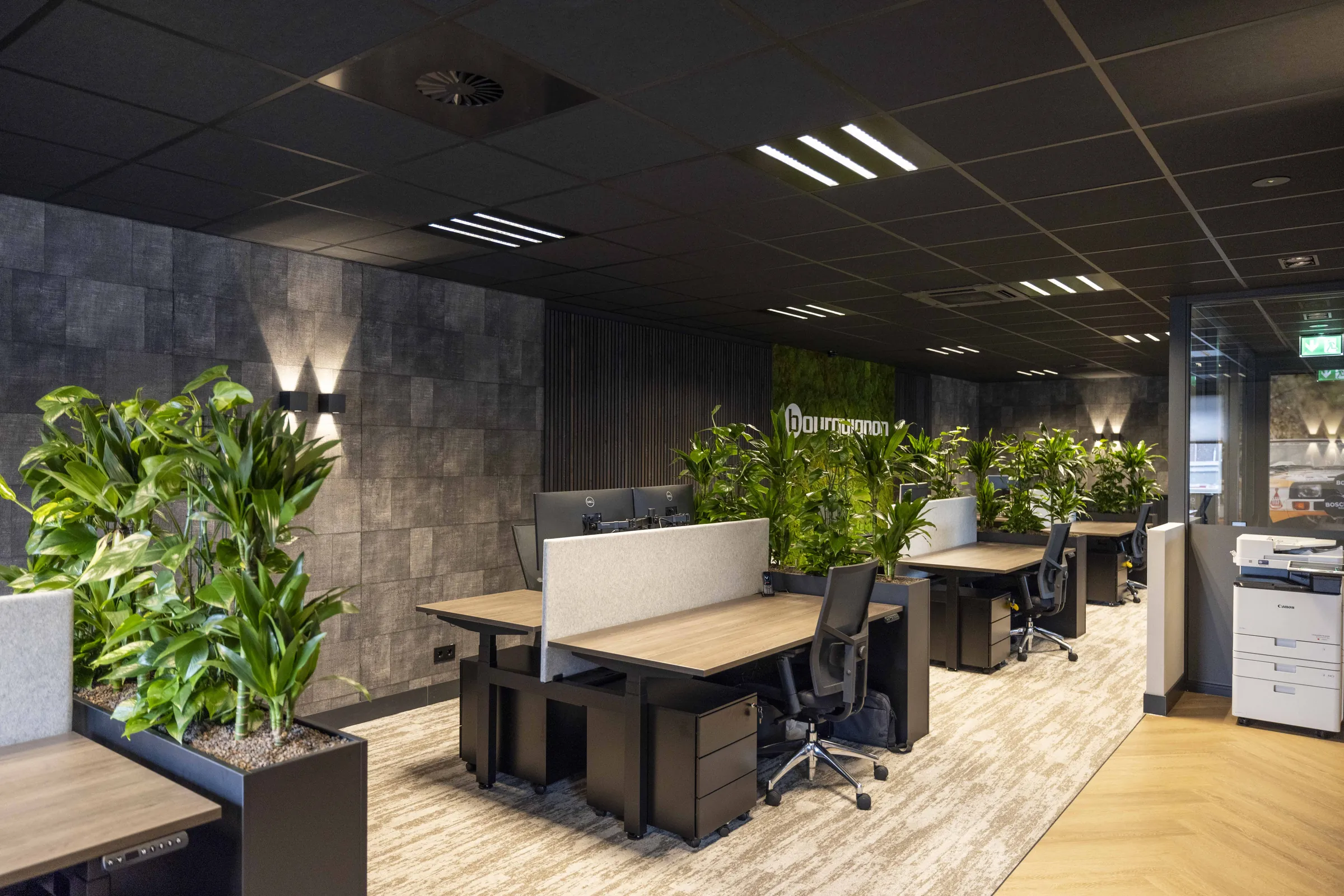 Open kantoortuin met veel planten, donker plafond en zit-sta werkplekken