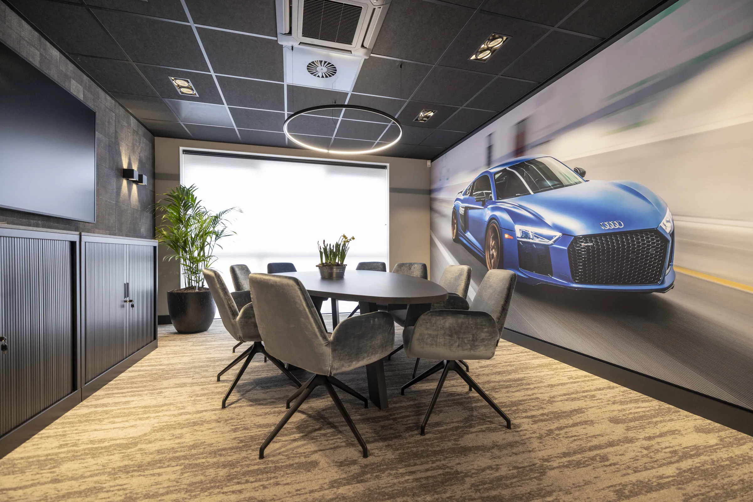 Vergaderruimte met ovale tafel, ronde lichtcirkel en wandvullende print van een blauwe sportwagen