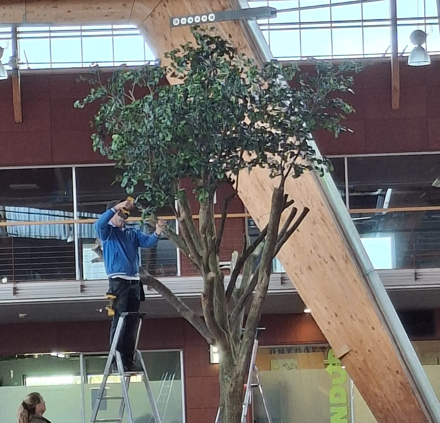 De kunstboom wordt op het plein in elkaar gezet, met iemand op een ladder in de kruin