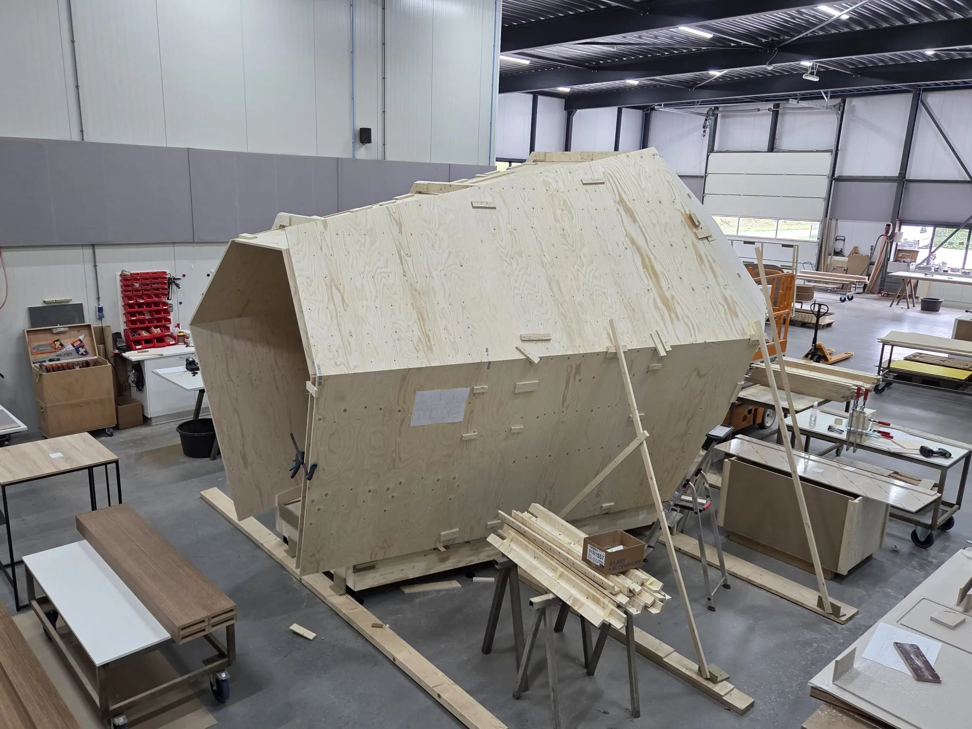 Een zeshoekige hut van plaatmateriaal in aanbouw in de werkplaats, van opzij gezien