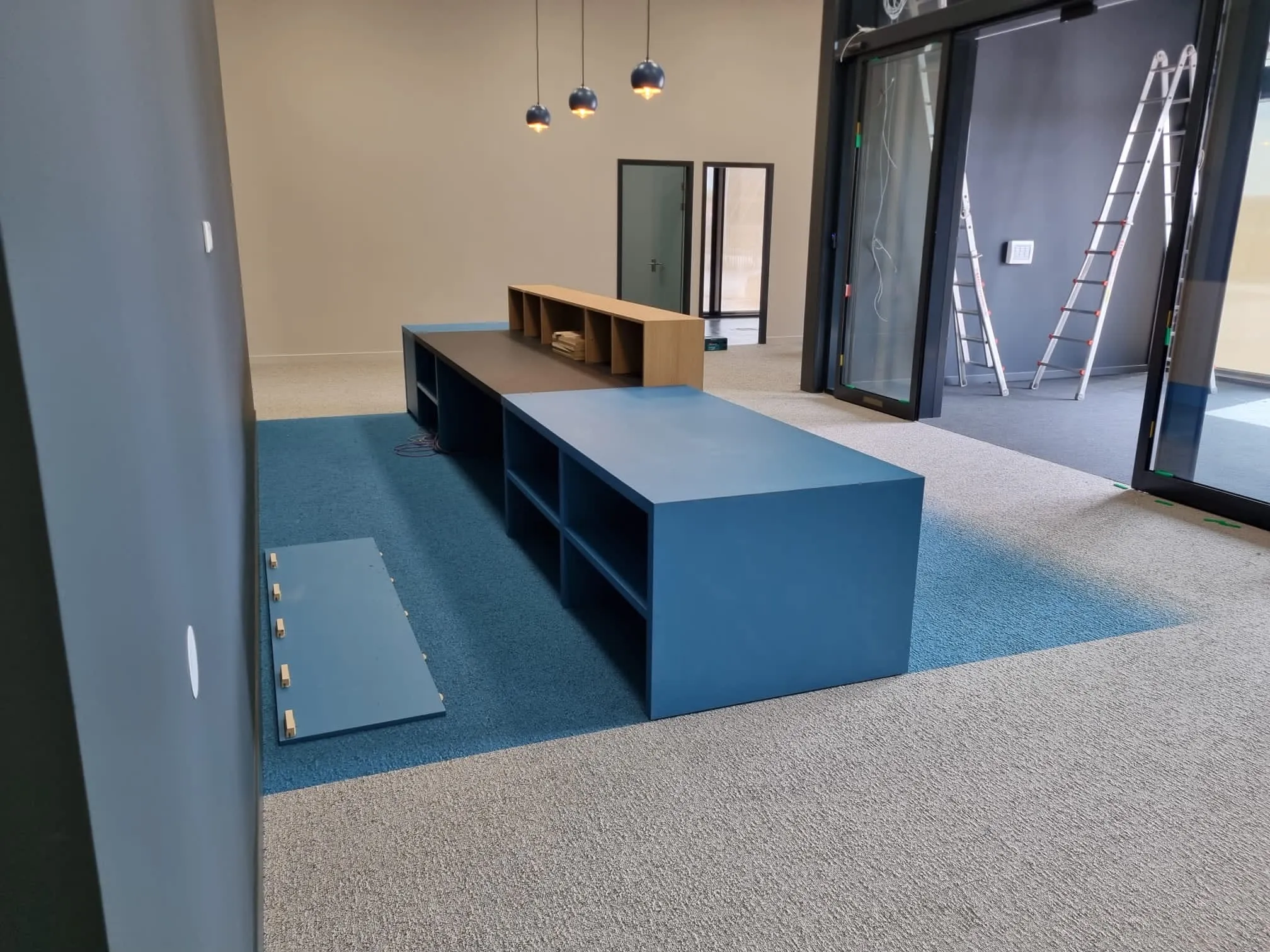 De blauwe ontvangstbalie in montage, met een los paneel op de vloer en ladders bij de entree