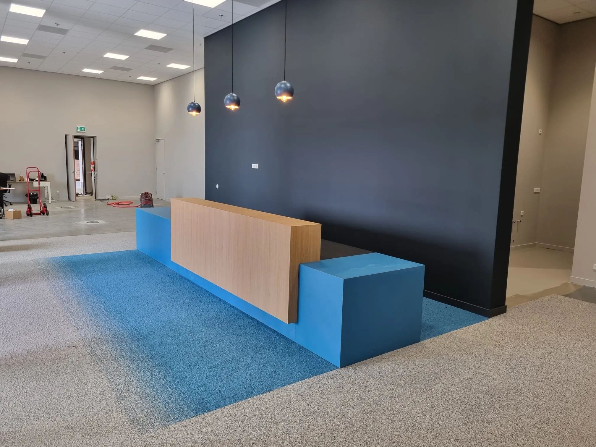 Ontvangstbalie met eiken front en blauwe blokken op blauw tapijt, met drie bolvormige hanglampen