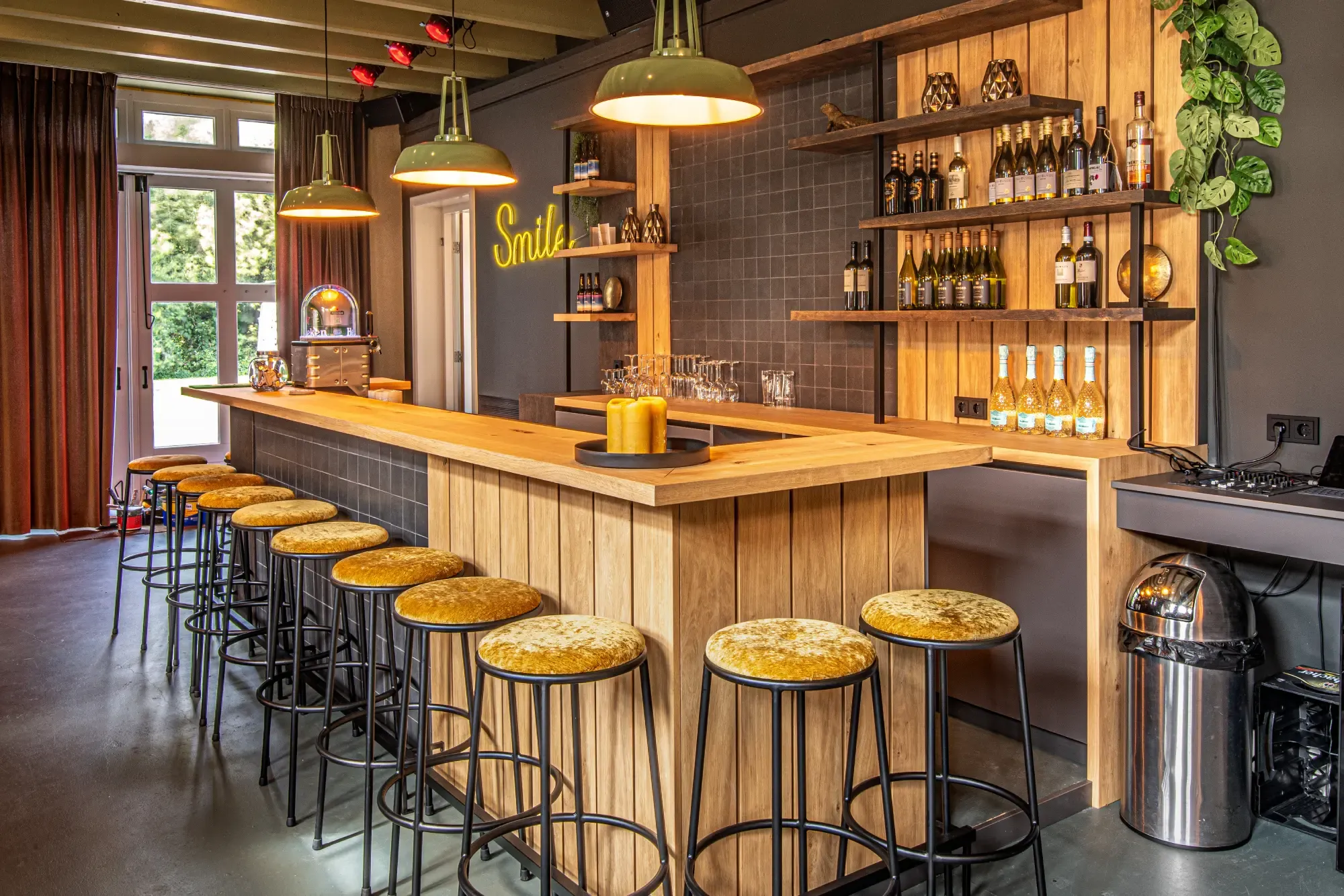De bar van Multiselect met een houten front, gele krukken, groene hanglampen en wandrekken vol flessen