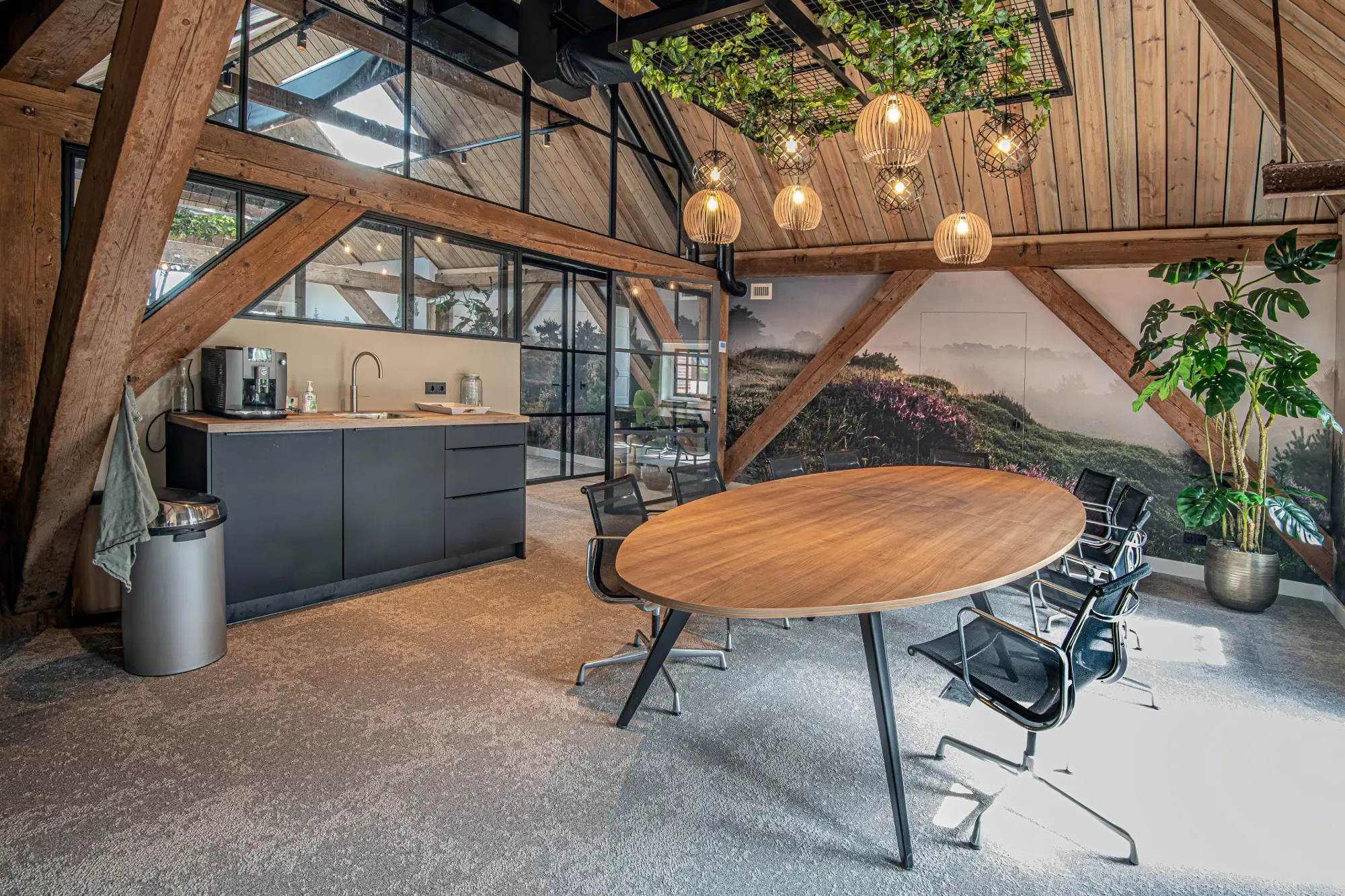 Een ronde vergadertafel onder de houten kap, met een pantry en een landschapsbeeld op de wand