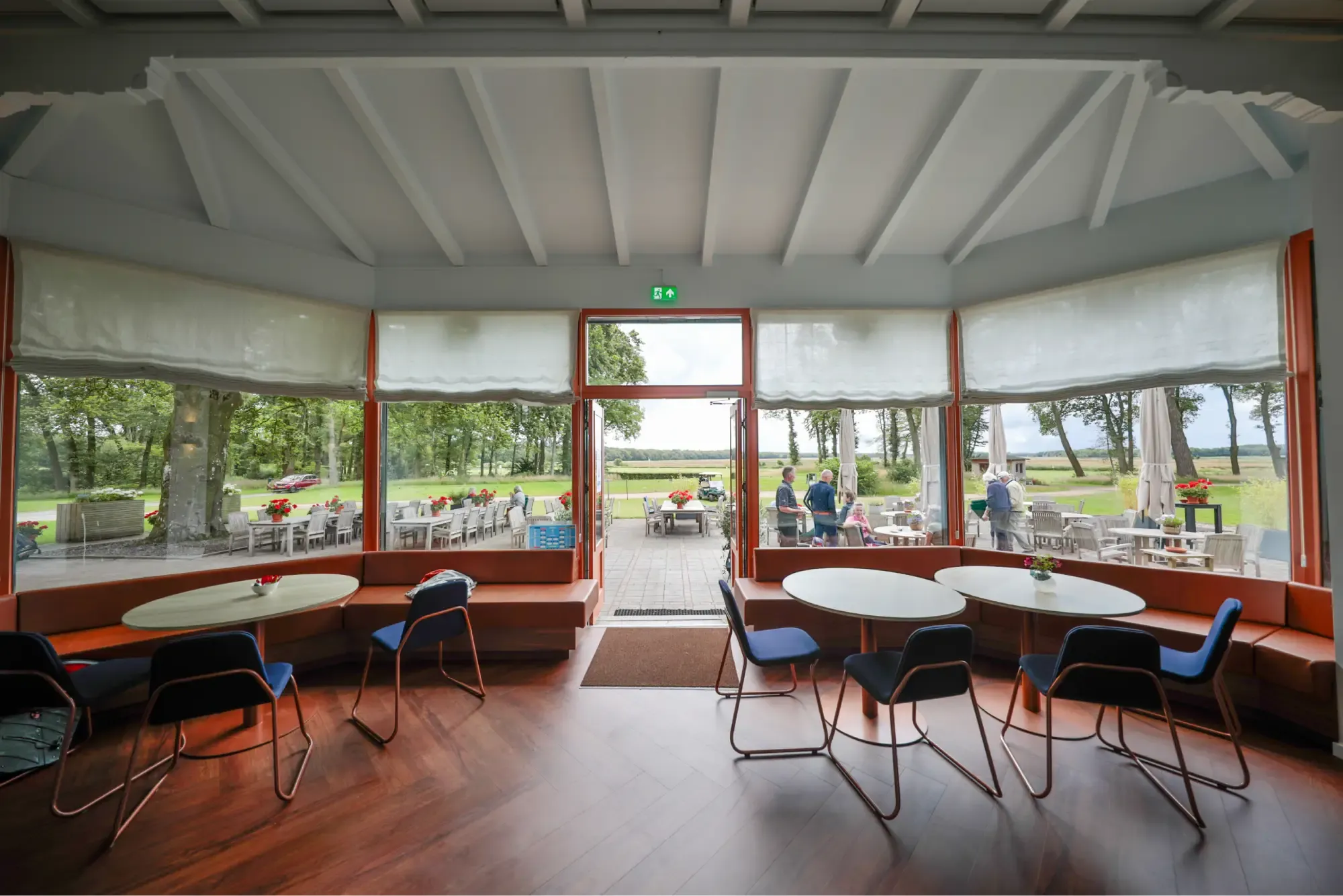 De serre met ronde tafels, stoelen en uitzicht op de golfbaan