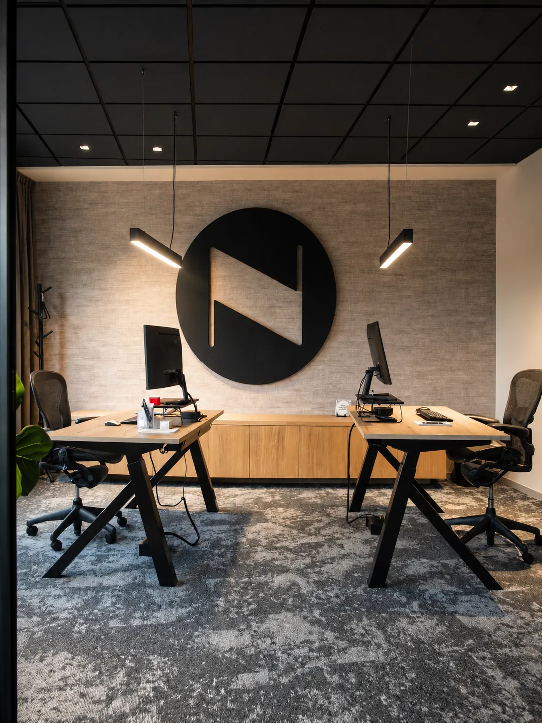 Werkkamer voor twee met houten bureaus op zwarte poten en een groot rond N-logo op de wand
