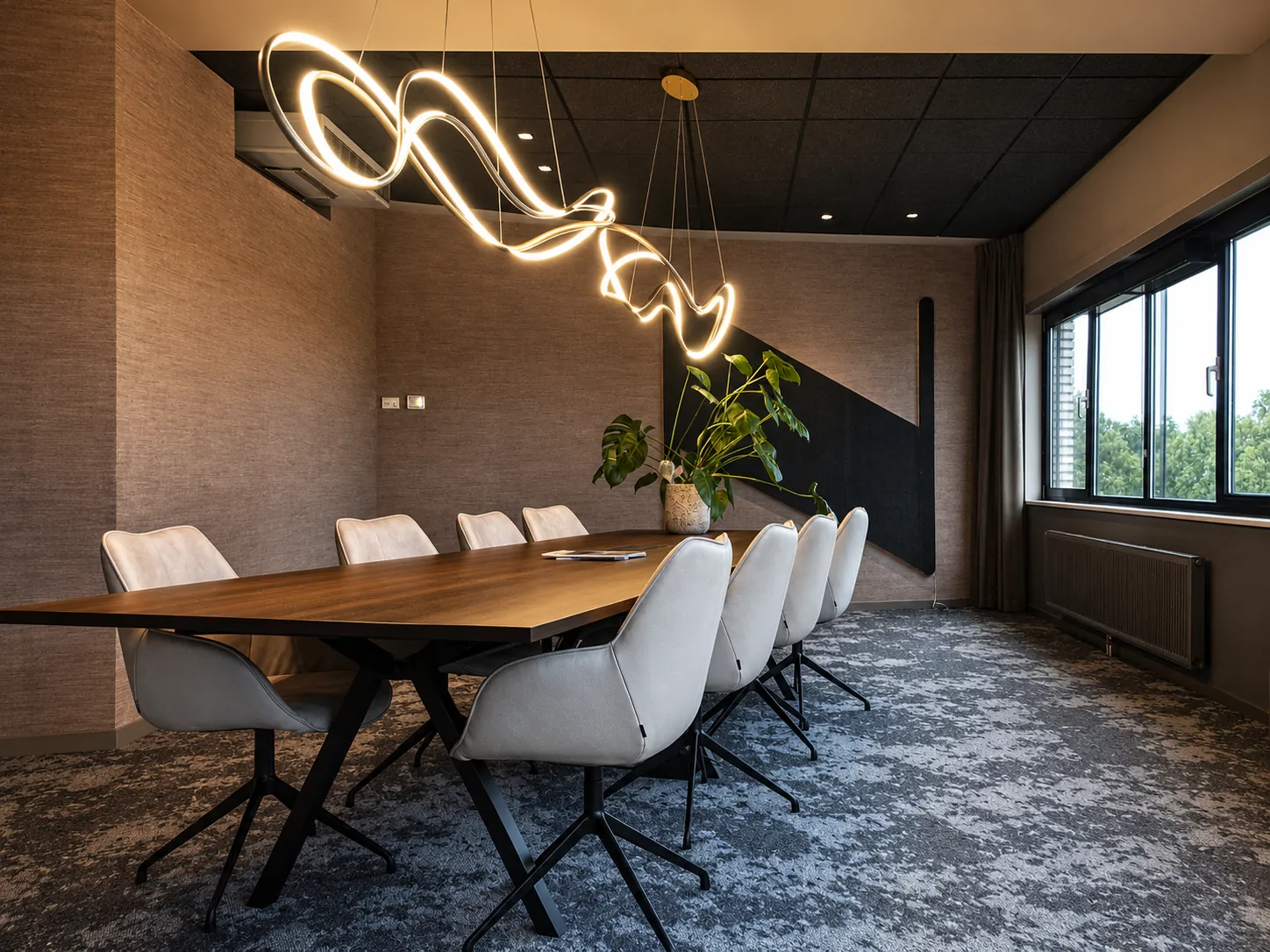 Vergaderzaal met een lange donkere tafel, lichte leren stoelen en een golvende ledlamp boven de tafel