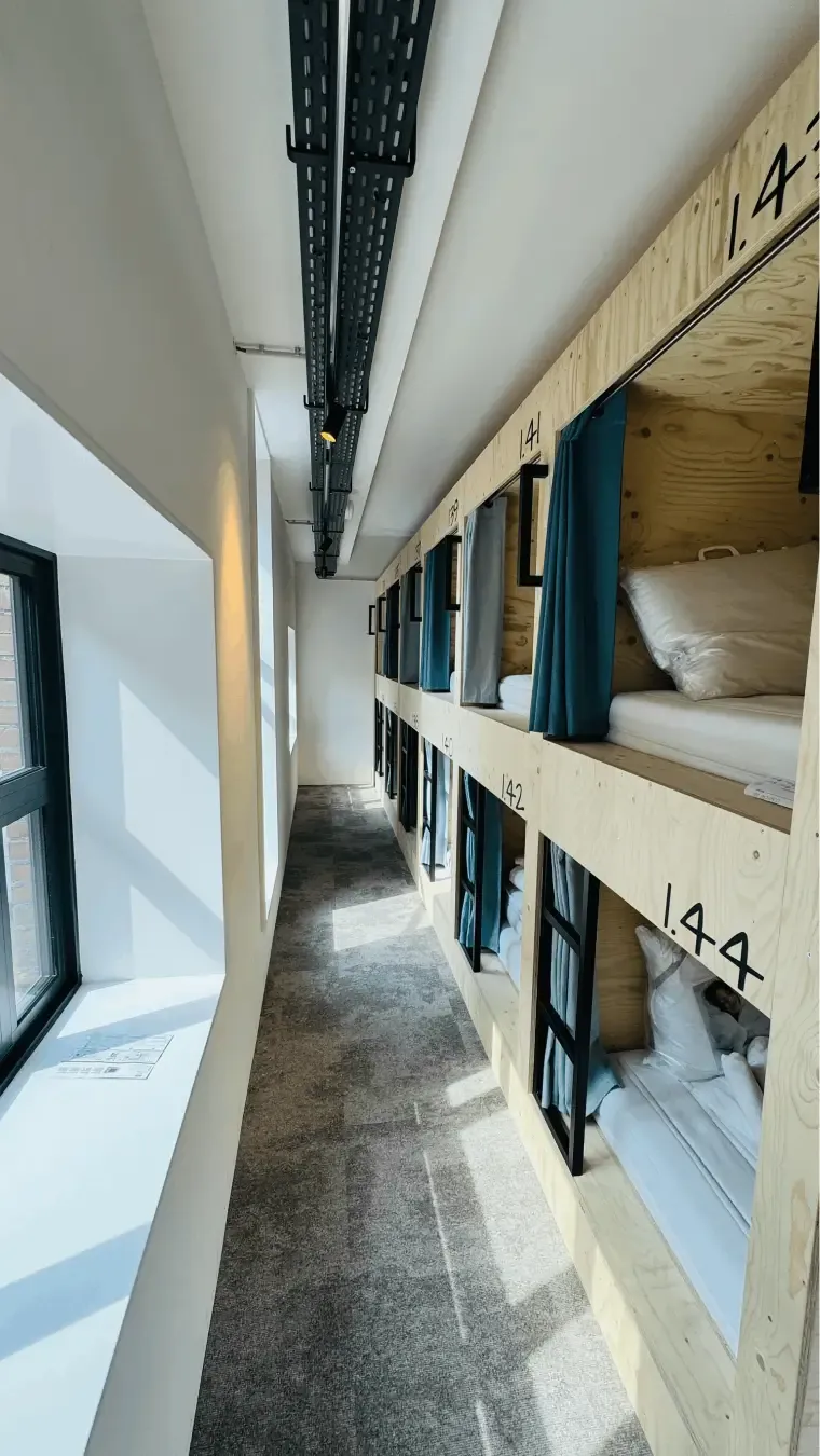 Een gang met genummerde houten slaappods bij PJ's in Groningen