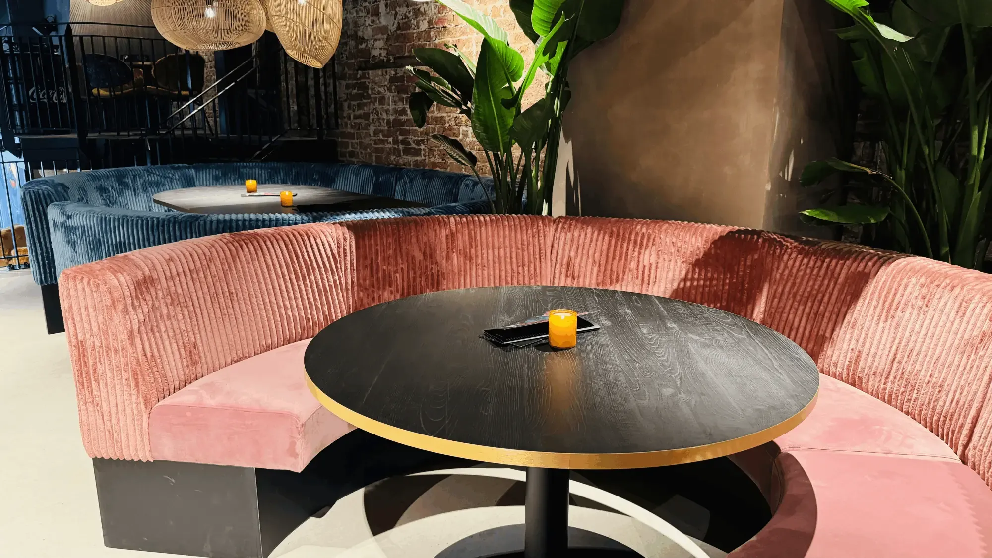 Een ronde zitbank in roze ribfluweel rond een zwarte tafel