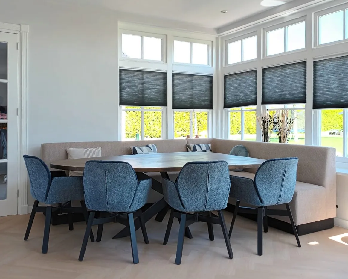 De eethoek in de erker van iets verder weg, met de blauwe stoelen en een bank langs de wand
