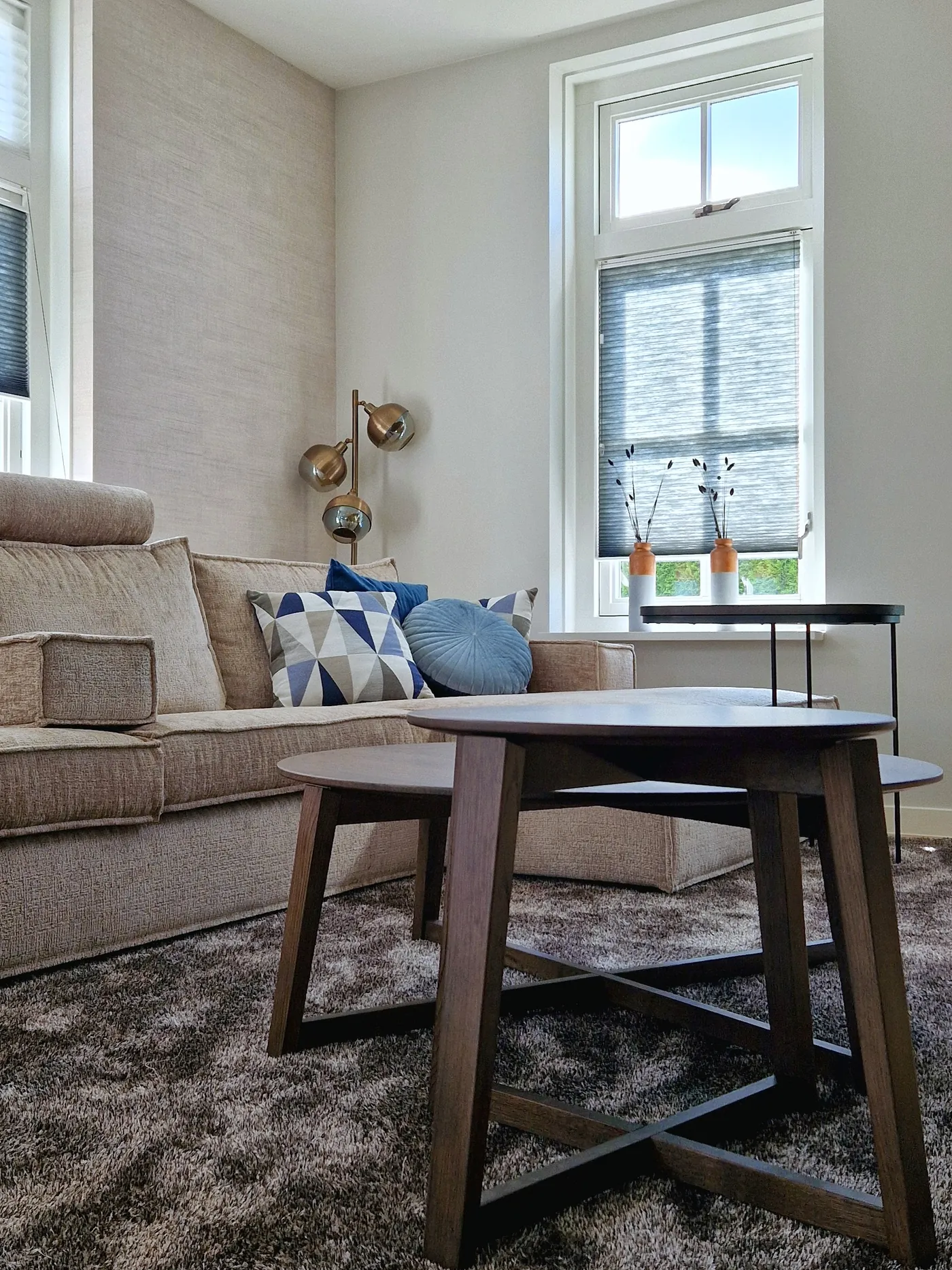 Twee ronde houten salontafels naast de hoekbank, met kussens in blauw en grijs