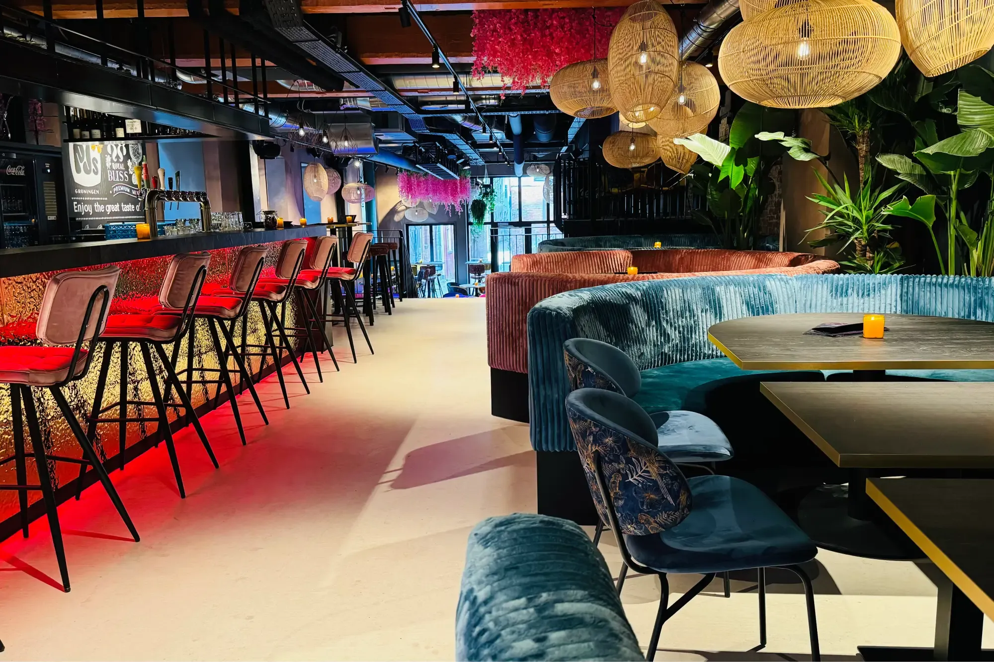 De bar van PJ's in Groningen met rood licht onder de bar, hoge krukken en ronde banken in roze en blauw ribfluweel