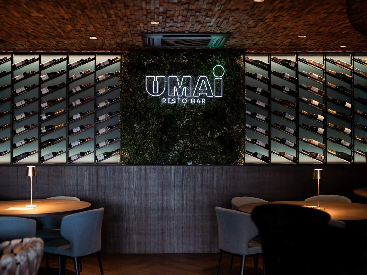 Umai Resto Bar in Urk: verlichte wijnwand, moswand met neonlogo en tafels met een eigen lampje