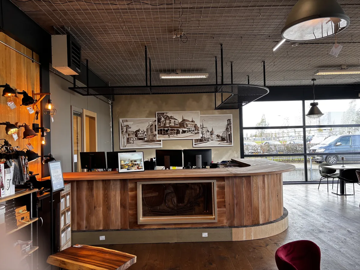 Een gebogen bar van hout met een verlichte nis in het front, met daarachter beeldschermen, oude stadsfoto's aan de wand en een rek aan het plafond